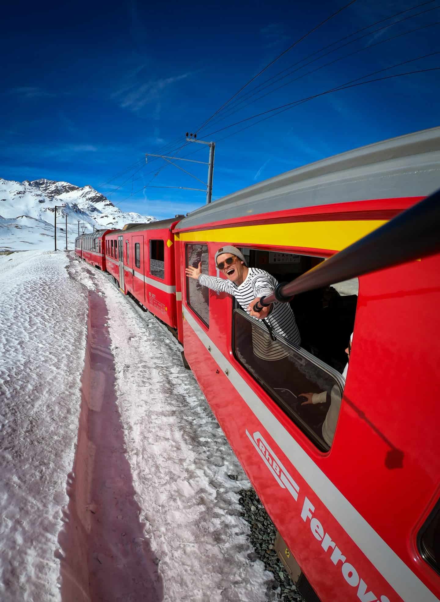 Man leaning out of scenic red Swiss train.