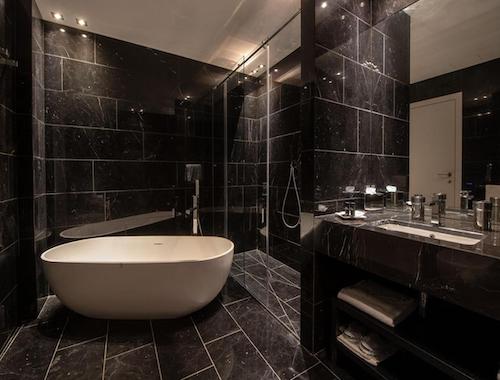 Sleek black marble bathroom with a walk-in shower and standalone tub at Hotel Gabbani in Lugano.