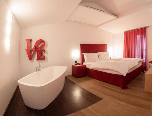 Freestanding bathtub in a modern hotel room with a red bed at Hotel Gabbani in Lugano.