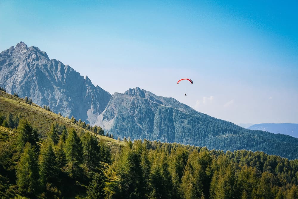 A skydiver with parachute open, floating above the mountains of Switzerland.