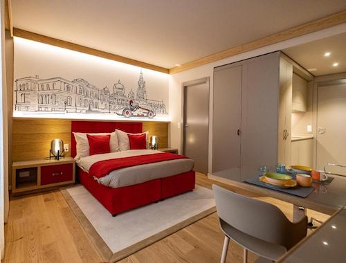 Stylish hotel room with red bedding, city artwork above the headboard, and wood flooring.