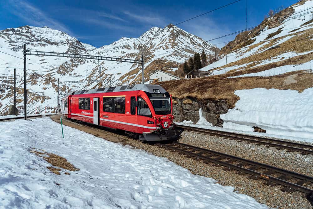 Red scenic train at Alp Grüm station surrounded by snowy mountains