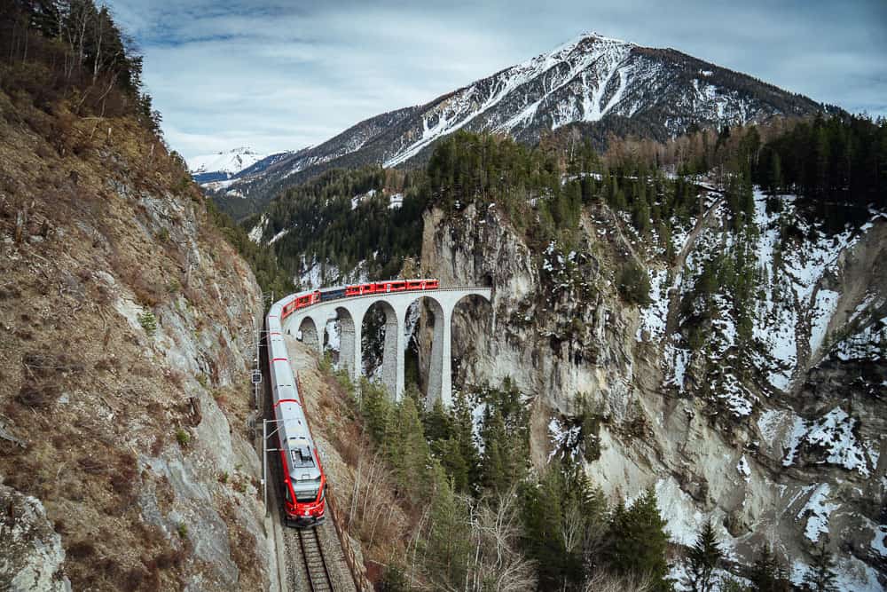 Red train crossing the Landwasser Viaduct with forest and mountain backdrop